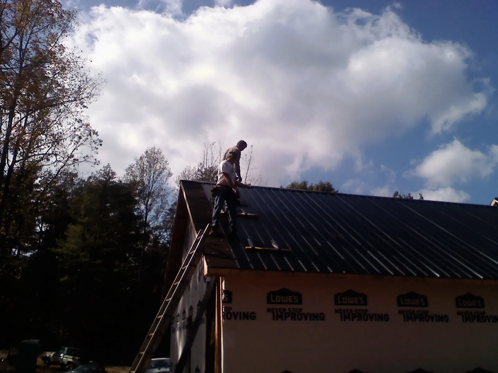 Roofer fastening dark metal panels high against a cloudy sky, from a Roof Inspection job in Warrensburg