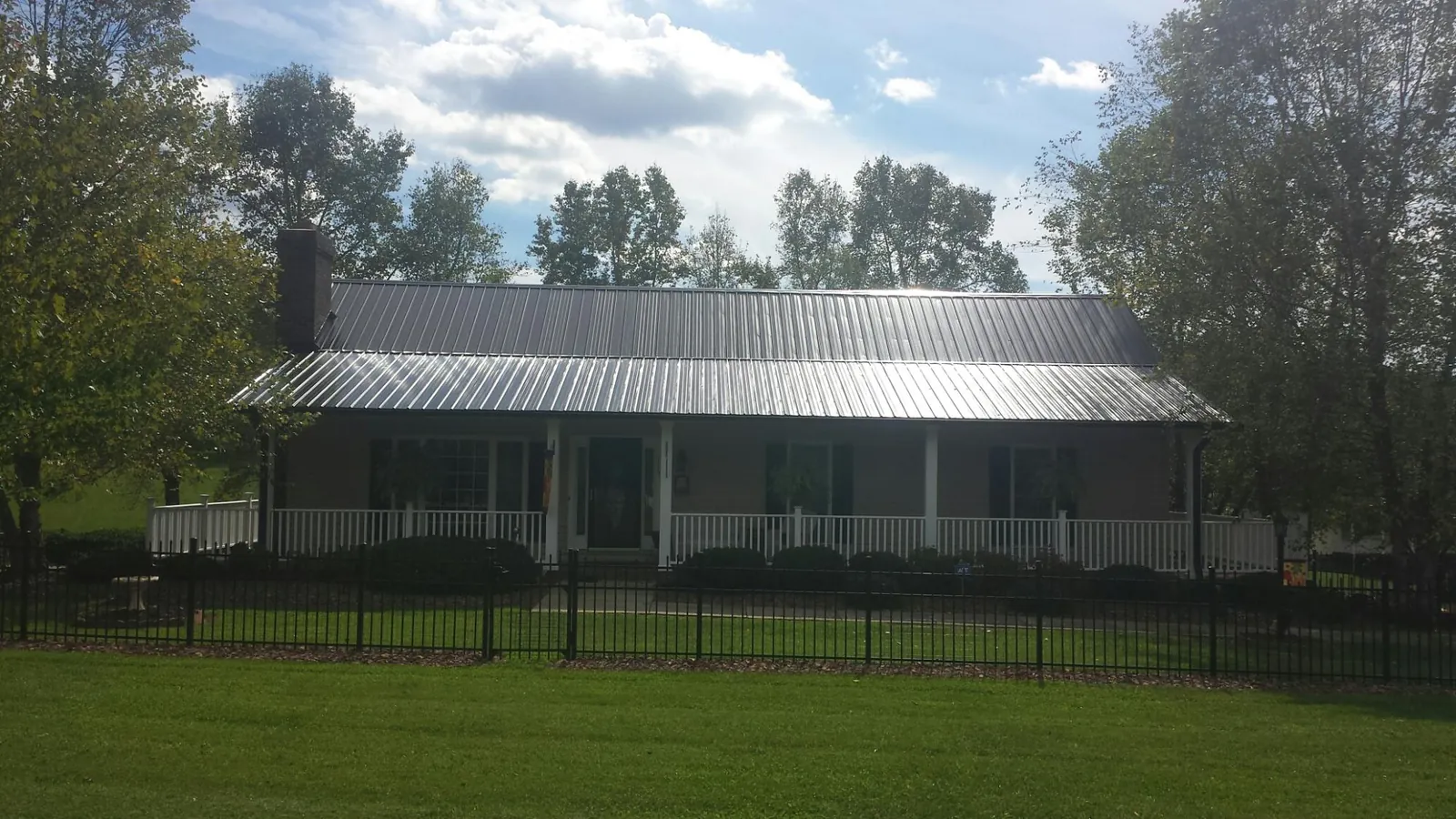 Gray metal roof on a brick ranch with a full width front porch — Gutter Guard Installation work by our crew in Warrensburg