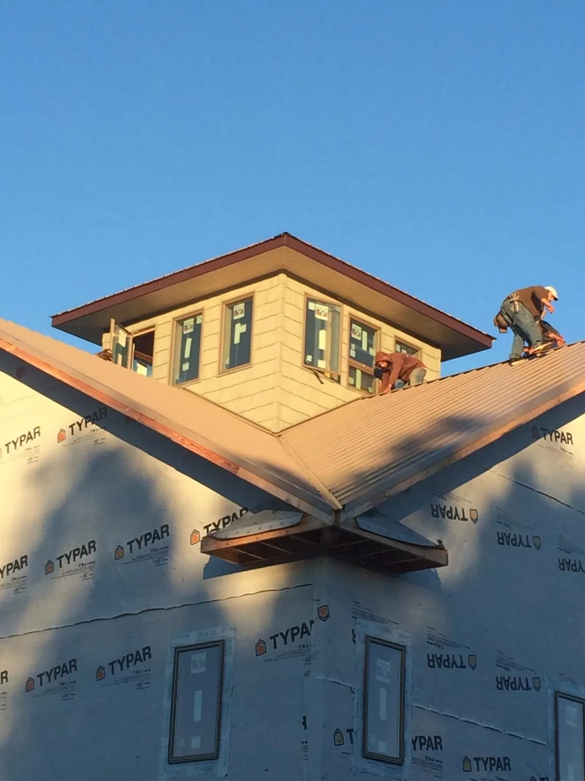 Roofers working around a rooftop cupola on a new metal roof at sunset — Roof Waterproofing in Warrensburg by Roofing Brothers